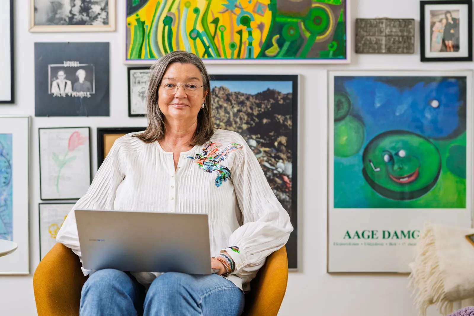 Birgitte Damgaard med sin computer foran en væg fuld af kunst